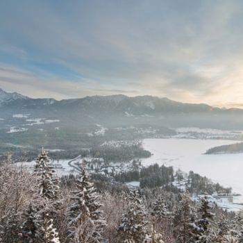Wim-Hof Winterlandschaft mit verschneitem Wald, zugefrorenem See und Sonnenaufgang über Bergkette